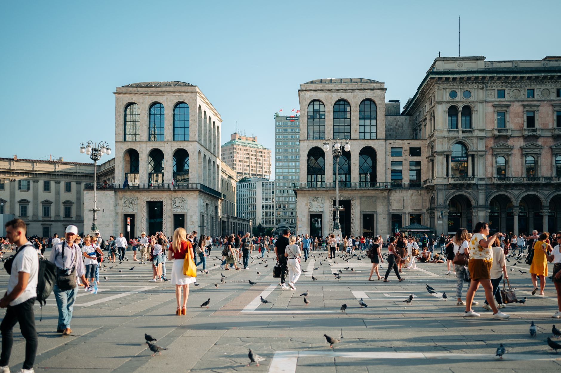 Bustling scene at Milan's Museo del Novecento with visitors and pigeons under a clear sky. — Coronavirus disease 2019