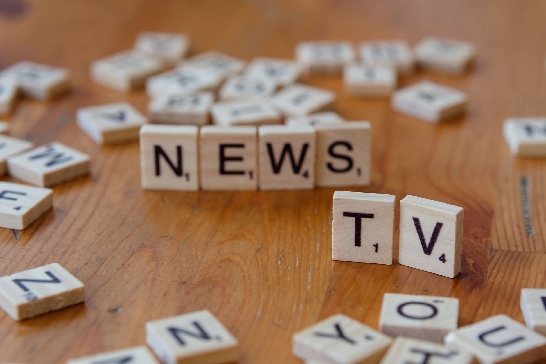 Close-up of Scrabble tiles spelling News and TV on a wooden surface. — NV Casino: Your Mobile Hub for Quick Wins and Instant