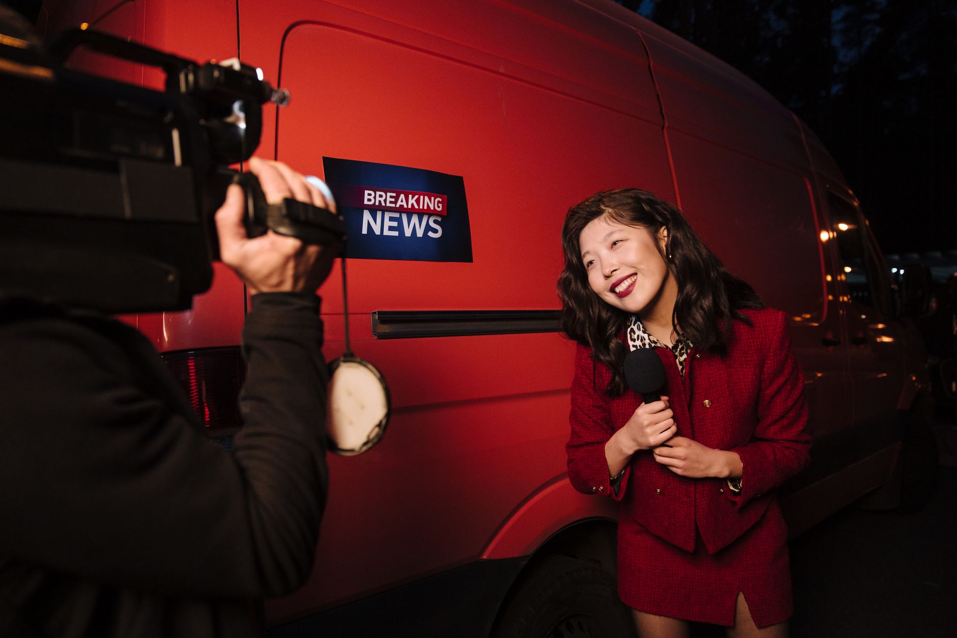 Asian female reporter in a red blazer reporting live on the news outdoors in the evening. — Spin Million Casino cashback et a